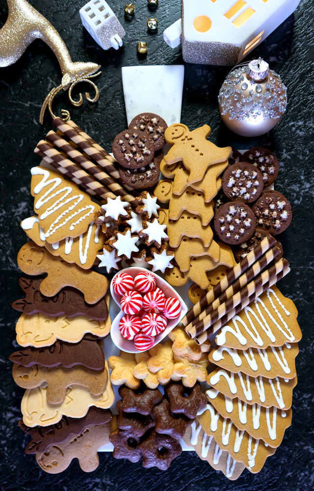 Happy Holidays Christmas large dessert grazing platter charcuterie board with gingerbread, chocolate and shortbread cookies with black and gold theme flat lay.